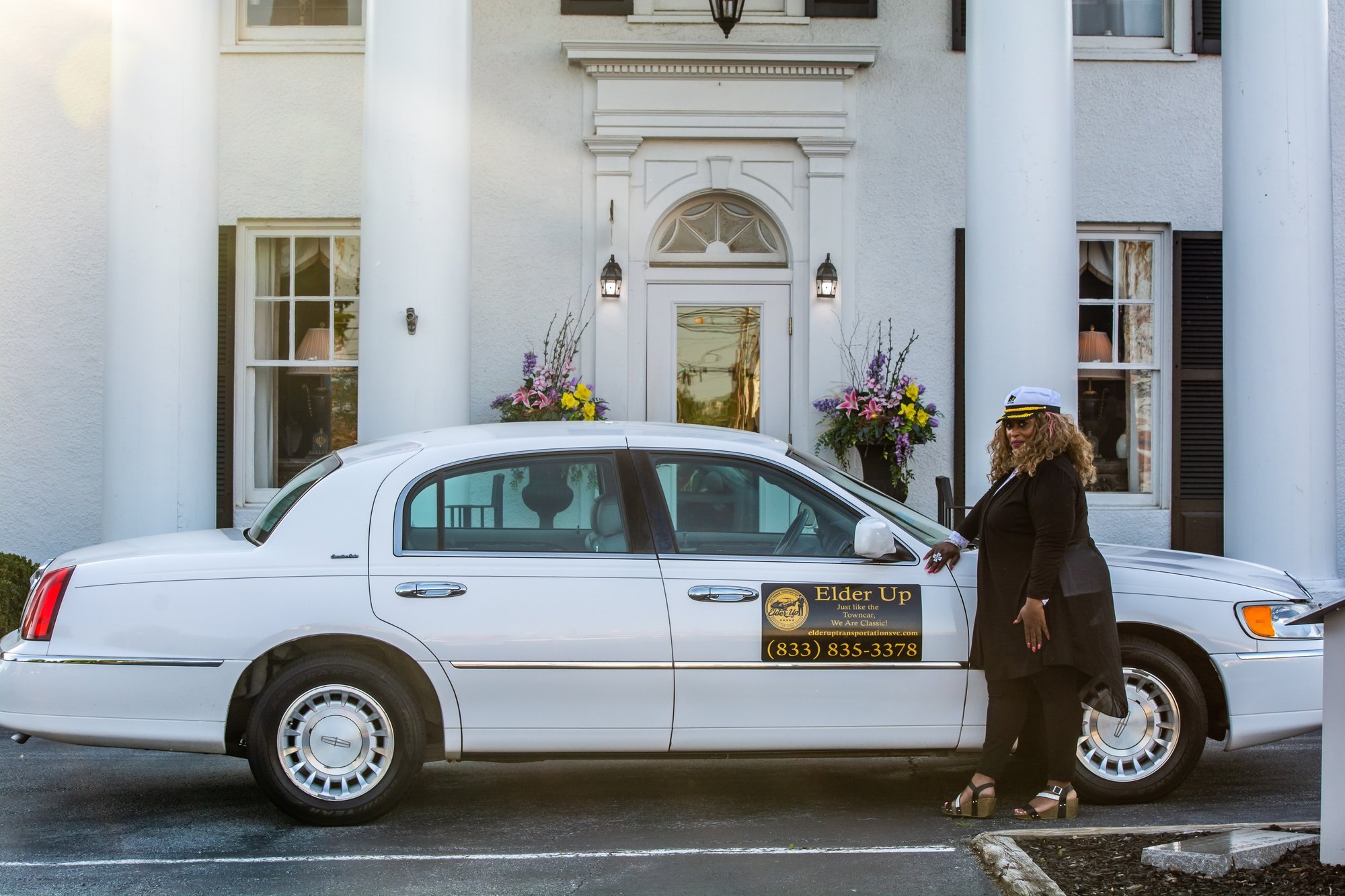 Robyn S. Chavis, founder of Elder Up, in chauffeur uniform beside the Elder Up Town Car
